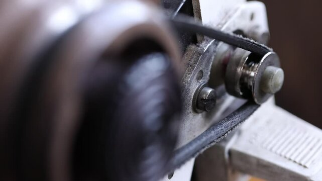 Macro close-up of a sewing machine's flywheel spinning. The camera rack focuses to the rotating belt and pulley system, revealing the machine's inner mechanical motor workings.