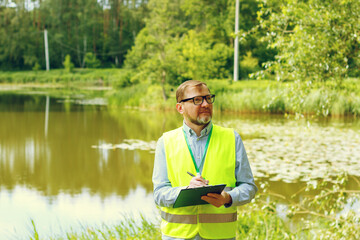 Male ecologist. Biologist is conducting research into the ecological state of nature near a body of water.