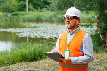 Forestry engineer records the results of monitoring the condition of trees near a reservoir....
