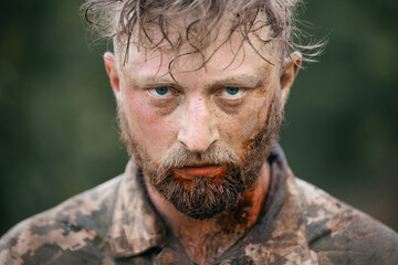 Close-up portrait of a wounded soldier covered in blood during combat. The soldier's face is...