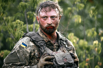 Tired Ukrainian soldier after the battle in a camouflage and blood in the forest. Concept of...