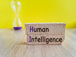 Concept word Human intelligence on brick blocks. Beautiful wooden table yellow background. Hourglass. Business concept