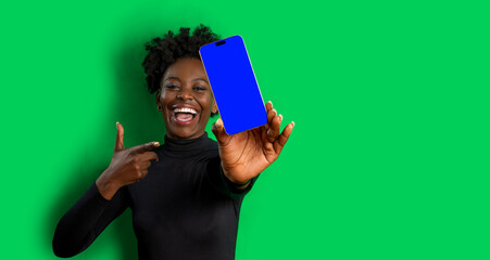 Smiling woman showing smartphone with blank screen on green background. Black female portrait with...