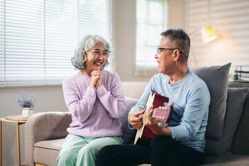 Asian Older Couple Enjoying Music at Home Happy Asian Man Playing Guitar for His Smiling Wife Relaxing on the Sofa Together