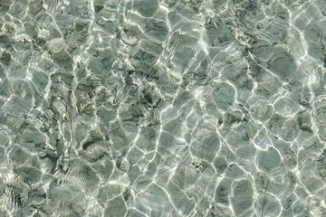 "Close-up of crystal clear shallow sea water with natural sunlight reflections creating abstract wave patterns – perfect for backgrounds or nature concepts."