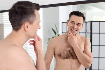 Smiling man after shaving looking at mirror in bathroom