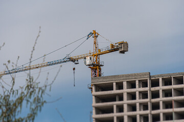 Overcast daylight image of a construction site with an extended yellow crane lifting metal...