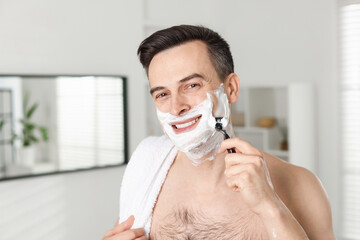 Smiling man shaving with razor at home
