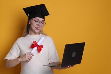 Happy student with diploma and laptop after graduation on orange background