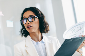 Confident businesswoman in formal attire presenting data at a modern office workplace during a...