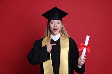 Happy student pointing at diploma after graduation on red background