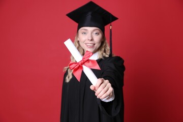 Happy student with diploma after graduation on red background, selective focus