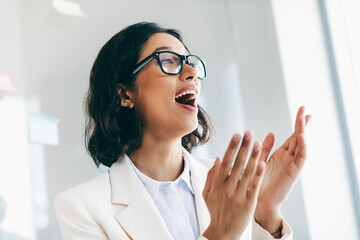 Confident businesswoman clapping in a modern office environment demonstrating recognition and...