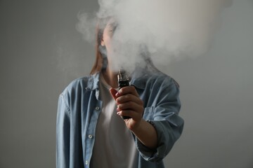 Woman using electronic smoking device on grey background