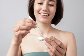 Woman taking contact lens out of case on light background, selective focus
