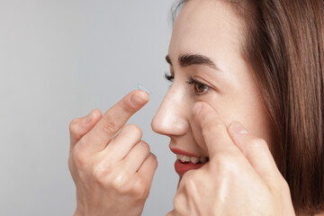 Woman putting in contact lens on light background, closeup