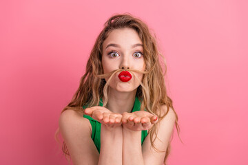 Young woman with playful expression and red lips in front of pink background, posing with a quirky...