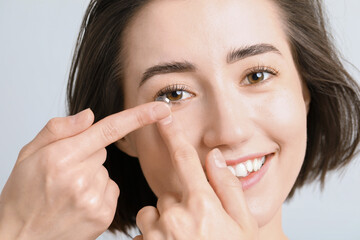 Woman putting in contact lens on light background, closeup