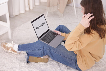 Cyber bullying. Upset teenage girl and laptop with text You Loser on floor indoors