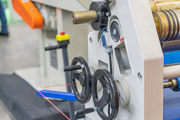 Industrial machinery, textile or paper production facility, metal components, gears, shafts, levers, red safety markings, factory floor, concrete ground, artificial lighting, shadows, blue garment, c