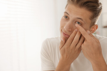 Man putting in contact lens at home. Space for text