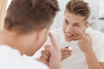 Man putting in contact lens near mirror at home