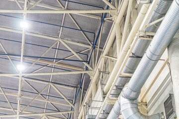 Industrial space with large open room, high ceilings supported by metal beams and pillars, network of multi-colored pipes, artificial lighting, concrete floor, documentary photography style, perspect