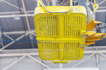 Large yellow machinery on a warehouse floor, industrial tower truck with multiple holes, concrete backdrop, fluorescent lighting, crane system or platform, cables, mechanical components, operational