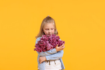 Little girl with bouquet of lilac flowers on yellow background