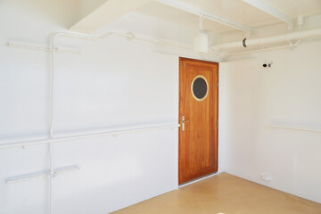 Wooden ship door with round porthole on white wall, seen on deck of a modern cruise or passenger vessel