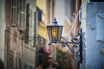 Vintage street lantern on iron bracket over narrow Marseille street with shuttered windows and flower pots