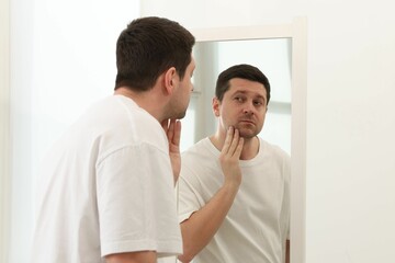 Handsome man looking at himself in mirror indoors