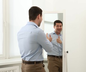 Handsome man showing thumbs up near mirror indoors