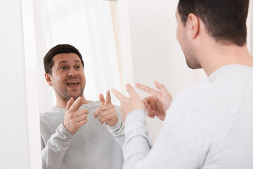 Handsome man looking at himself in mirror indoors