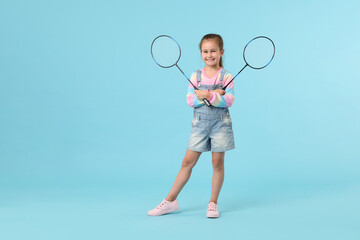 Little girl with tennis rackets on light blue background, space for text