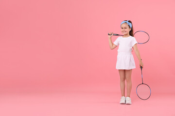 Little girl with tennis rackets on pink background, space for text