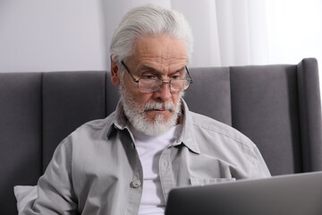 Senior man with vision problem using laptop on bed at home