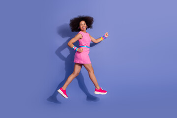 Energetic young woman in a stylish pink dress posing against a vivid purple background, embodying...