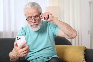 Senior man with vision problem using smartphone on sofa at home
