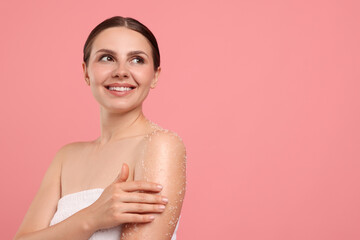 Smiling woman applying body scrub onto her arm against pink background. Space for text