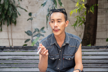 Stylish gay man sitting outdoors and smoking cigarette
