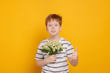 Boy with bouquet of beautiful lily-of-the-valley flowers showing thumbs up on yellow background