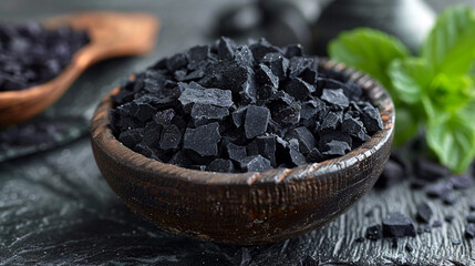 Black salt crystals in wooden bowl on dark slate surface with mint
