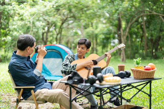 Family bonding during camping. Father and son enjoying music together outdoors.