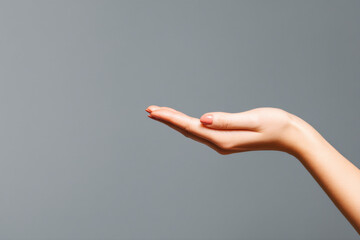 A right human hand with manicured nails extended against a plain gray background, palm facing upwards.