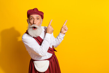 Elderly man in traditional Scottish attire surprised and pointing to the side on a bold yellow...