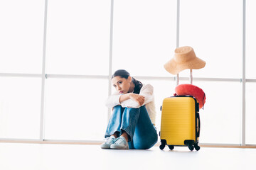 Sad woman sitting in airport terminal with suitcase and hat, portraying travel anticipation or...