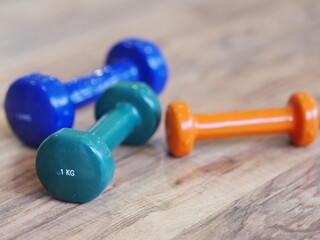 Three dumbbells of different colors and weights are on a wooden floor