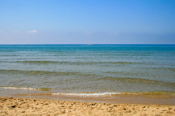 Obraz premium A quiet beach with clear water and a boat in the distance.