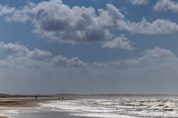 Skiveren, Denmark Sea, surf and clouds on the Skiveren beach near Skagen and people walking.